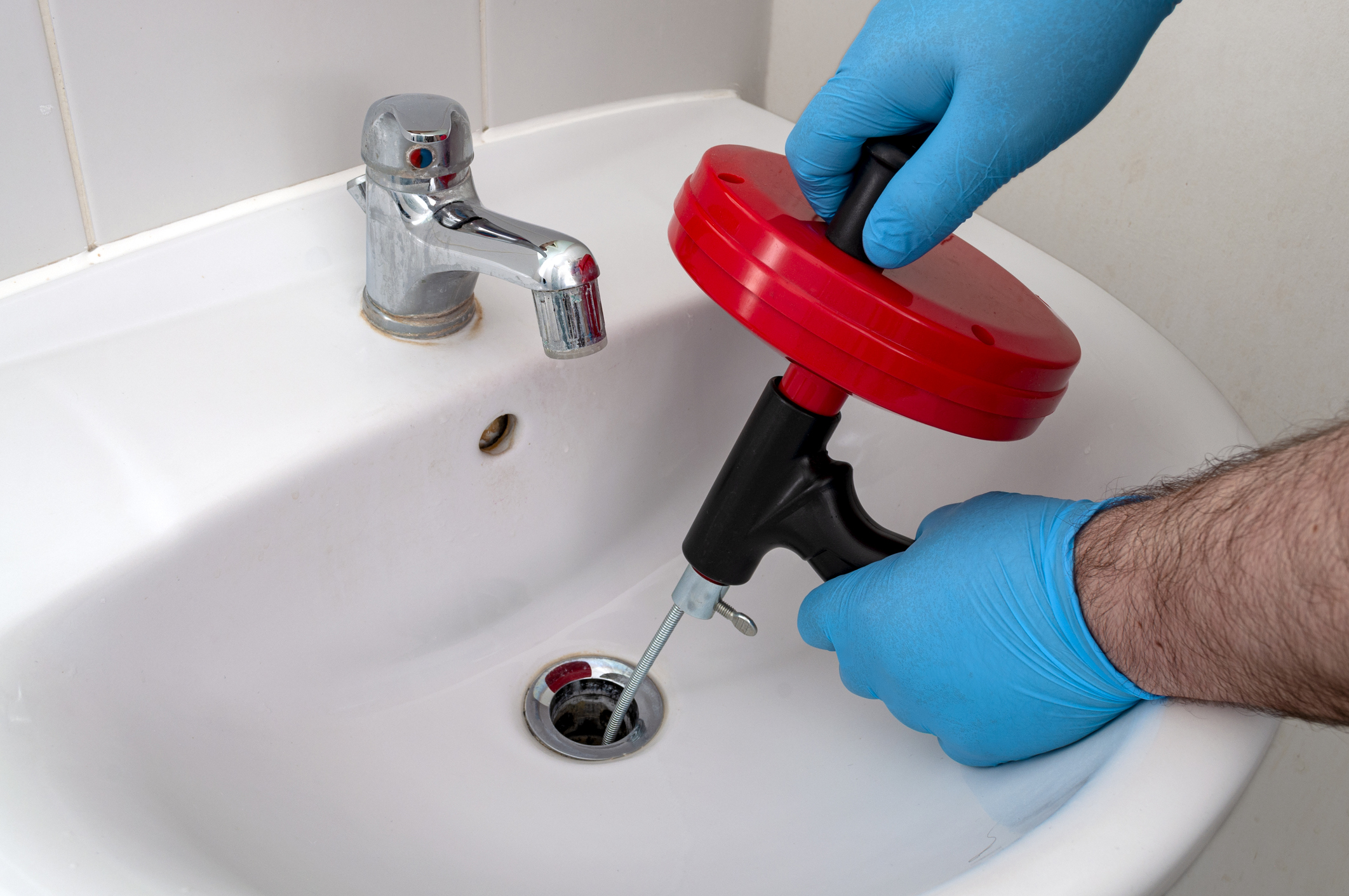Plumber using snake on clogged bathroom sink drain