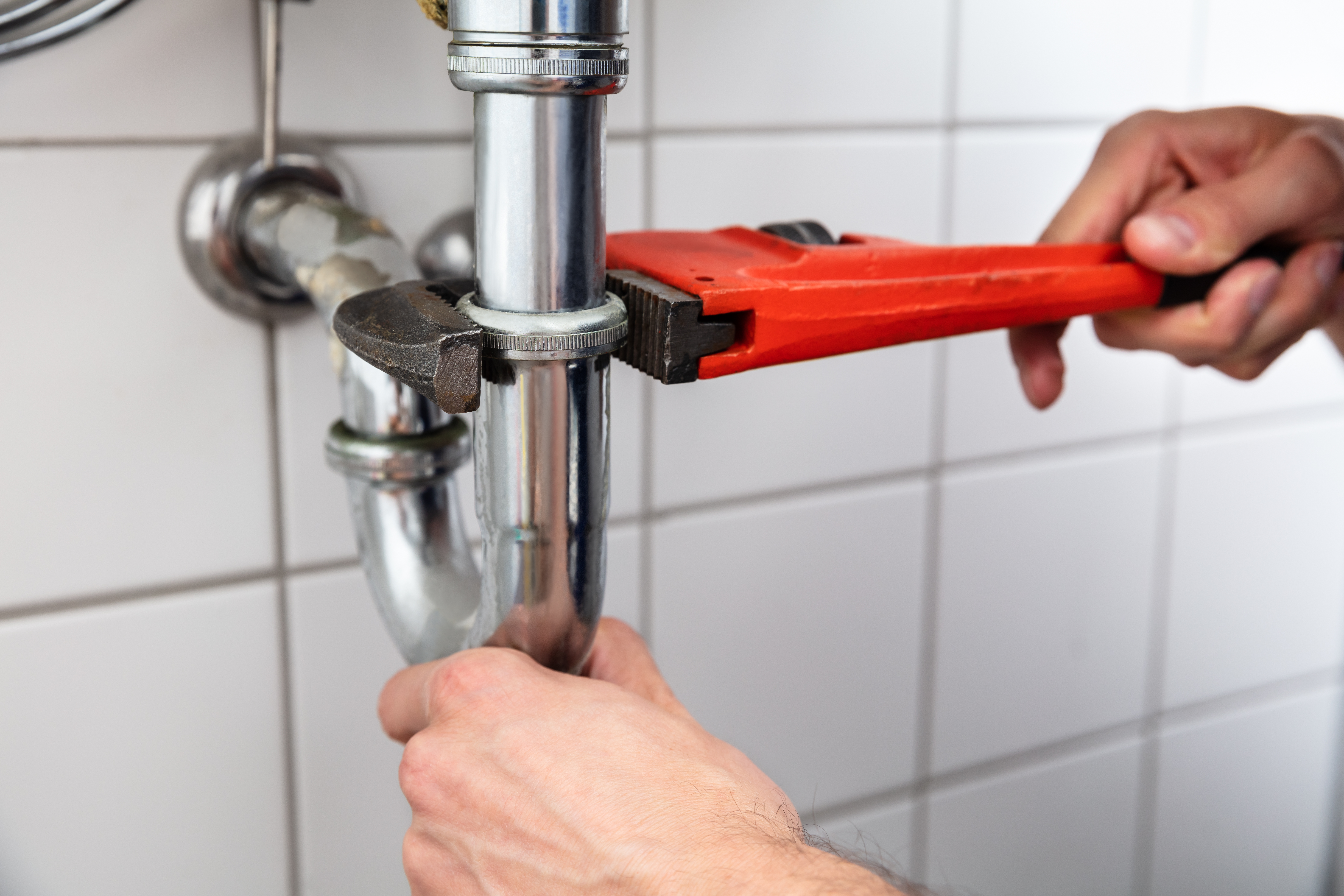 Plumber tightening a kitchen sink pipe connection with a red wrench