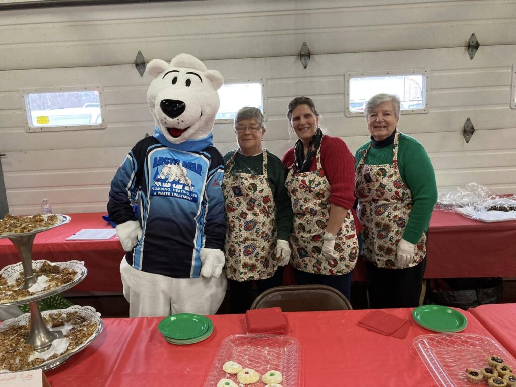 Arctic Bear mascot posing with three people wearing aprons with cookies on the table