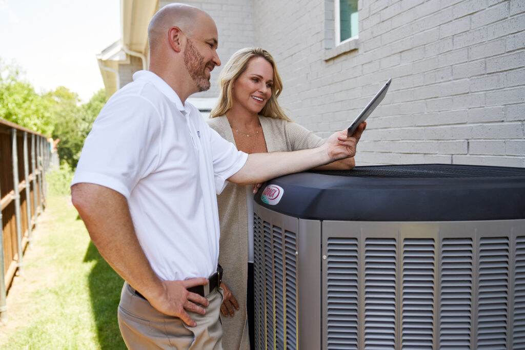 Lennox technician speaking with a woman outside her home, standing next to Lennox AC unit.